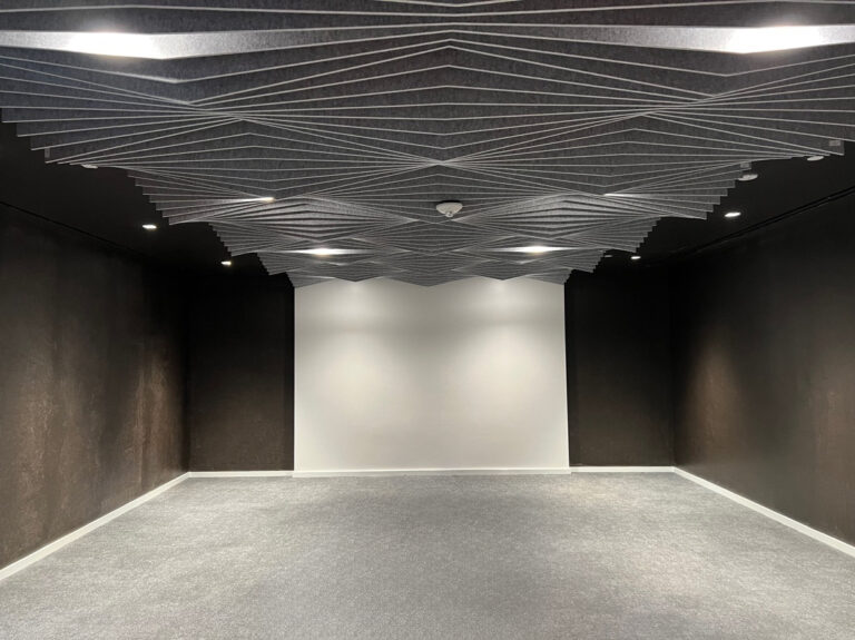 Straight-on view of the newly installed folded Soundcore baffle ceiling in Morning Fog over the empty Play/Test room, with charcoal walls and a white end wall